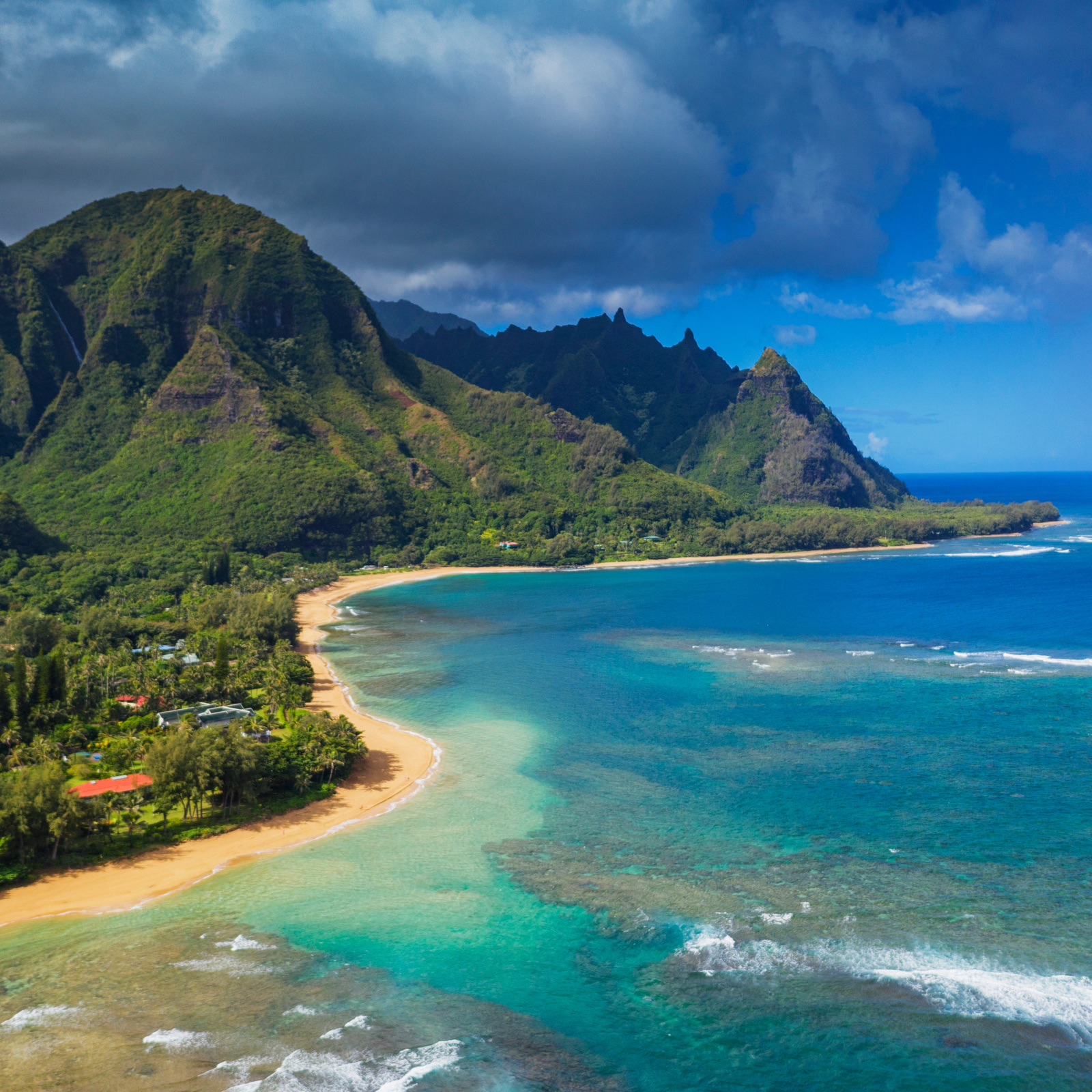 Aerial view of Kauaʻiʻs turquoise coastline, golden beach, and lush green mountains