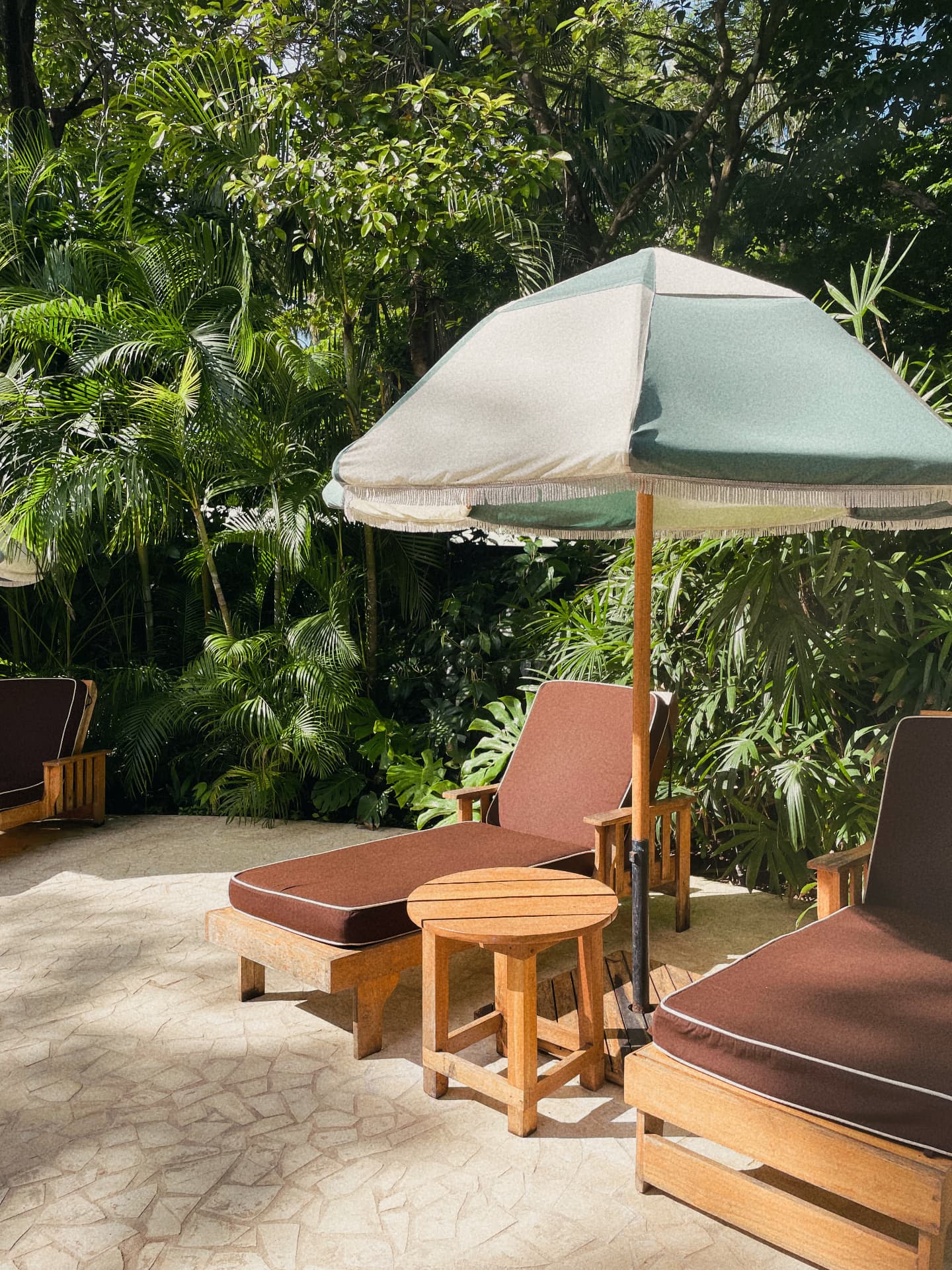 A shaded poolside lounge beneath a green and white umbrella in Hawaii